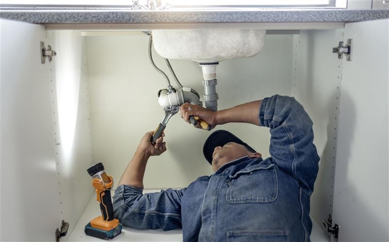 Plumber repairing pipes beneath a bathroom sink in Fort Lauderdale