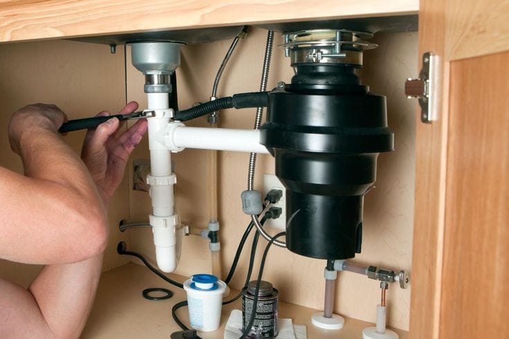 Plumber installing a garbage disposal beneath a kitchen sink in Fort Lauderdale