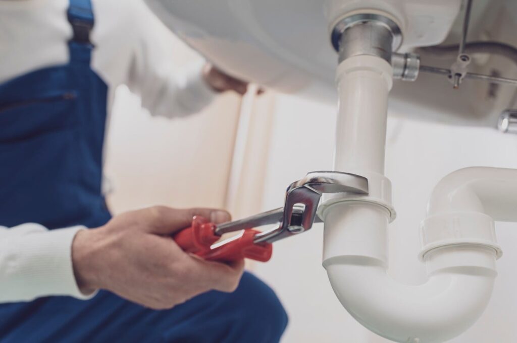 Plumber repairing a white drain pipe beneath a sink in Fort Lauderdale